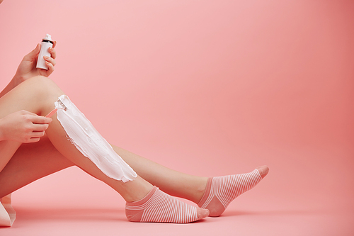 Young woman sitting on the floor, applying cream and shaving legs