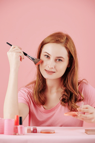 Portrait of beautiful young woman applying make-up when getting ready in the morning