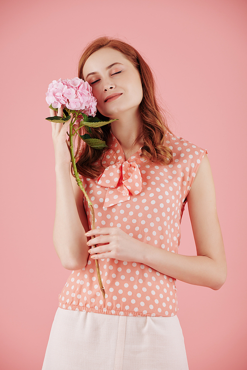 Pretty young woman enjoying tender petals of blooming pink flower