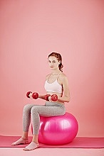 Pretty smiling young woman sitting on fitness ball with dumbbells in hands