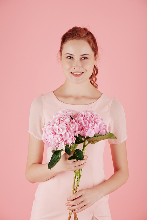 Portrait of young attractive red haired woman posing with pink blooming flower