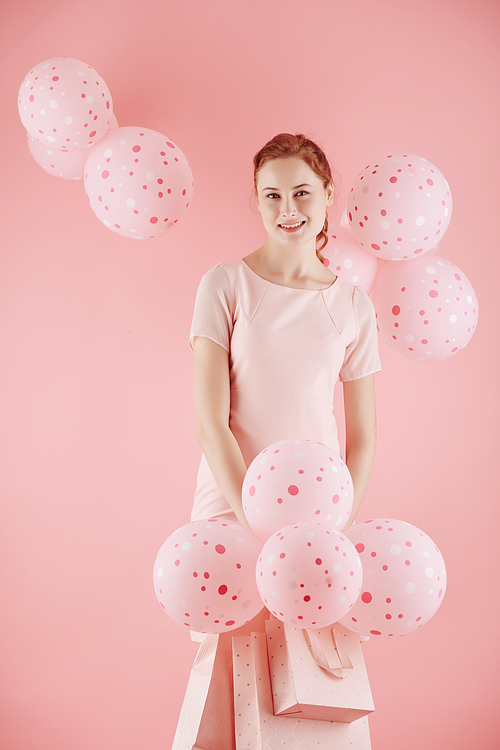 Cheerful young woman posing with pink balloons and shopping bags