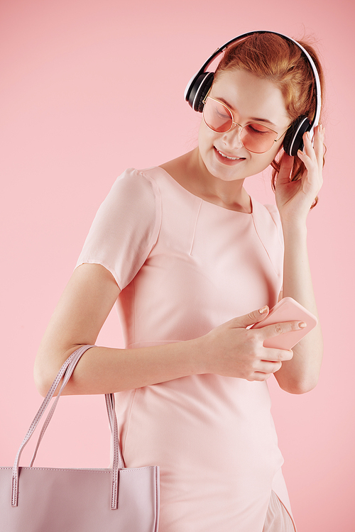 Portrait of cheerful young woman in pink outfit enjoying good music in headphones