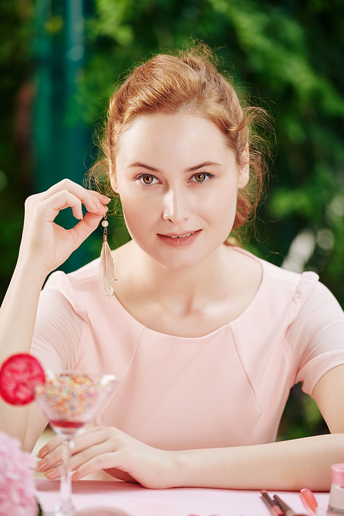 Pretty young red haired woman showing earrings she is going to wear for the occasion