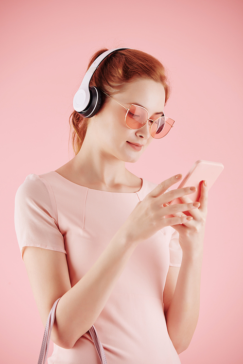 Smiling young pretty woman in headphones listening to music on her smartphone