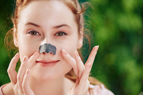 Smiling young woman applying nose strip to clean pores on her nose