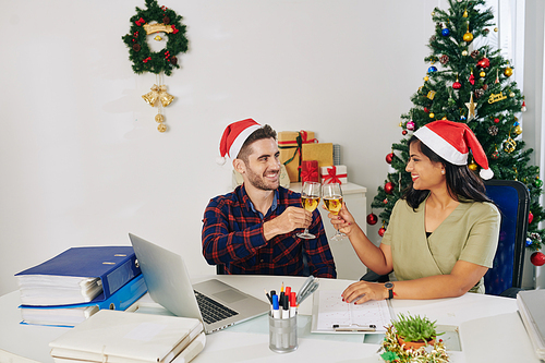 Young smiling colleagues celebrating Christmas in office and toasting with champagne glasses