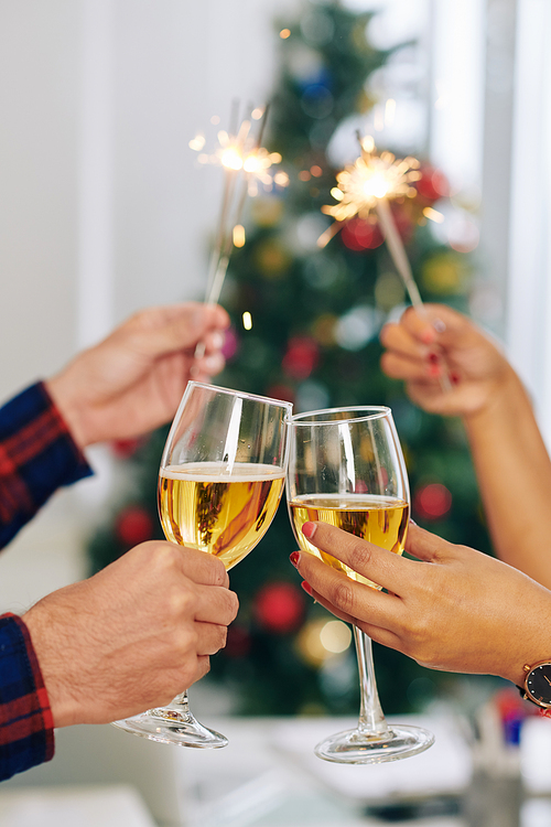 Hands of business colleague toasting with champagne glasses and burning Bengal lights when celebrating Christmas in office