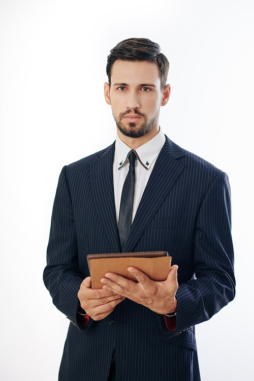 Serious handsome young entrepreneur standing with digital tablet in hands and looking at camera