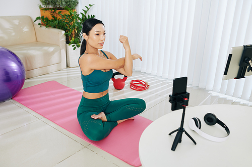 Female fitness blogger recording video how to stretch arms and warm up before intense training at home