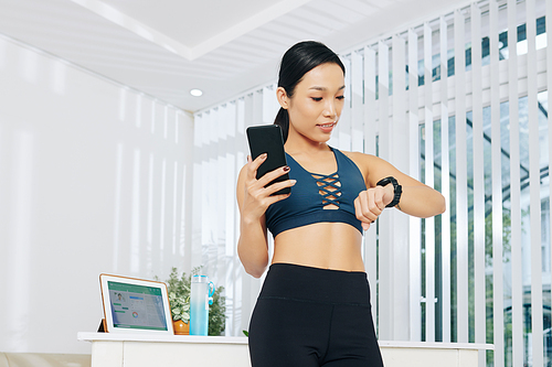 Pretty fit young Vietnamese woman checking smartwatch before working out at home