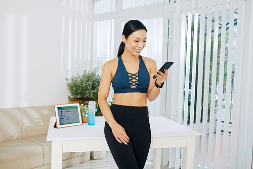 Smiling pretty Vietnamese fitness blogger checking comments and messages on her social media platforms