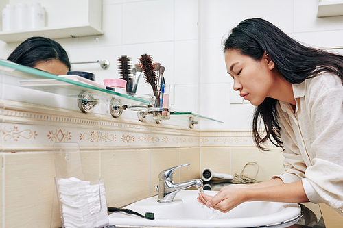 Beautiful young Chinese woman washing face in bathroom sink in the morning