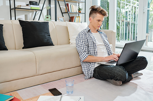 Concentrated college student sitting on floor with laptop and watching webinar online