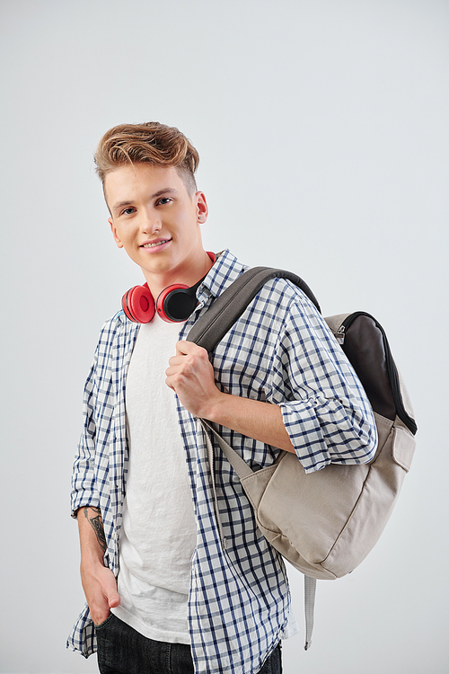 Portrait of positive college student with backpack looking at camera, isolated on light grey