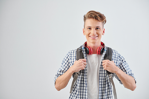 Portrait of positive teenage boy standing with backpack and headphones around neck