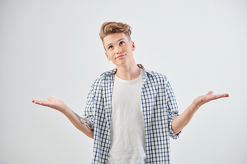 Studio shoot of confused clueless teenage boy making hands gesture and looking up