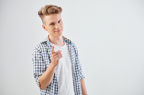 Positive confident teenager in plaid shirt pointing at camera, isolated on light grey