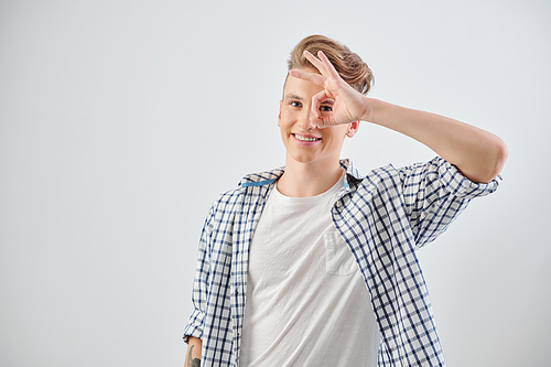 Portrait of smiling handsome teenage boy making ok gesture and looking at camera, isolated on light grey