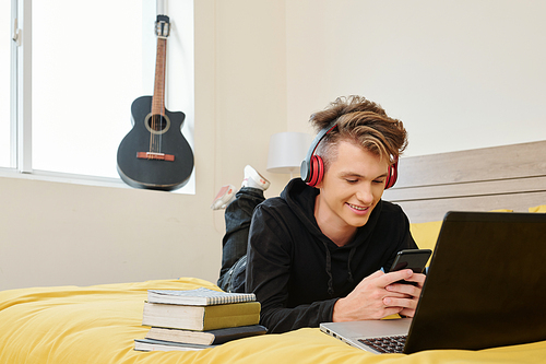 High school student lying on bed with smartphone and texting friends instead of getting ready for exams