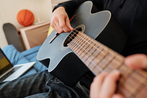 Close-up image of talented teenage boy playing guitar and singing at home