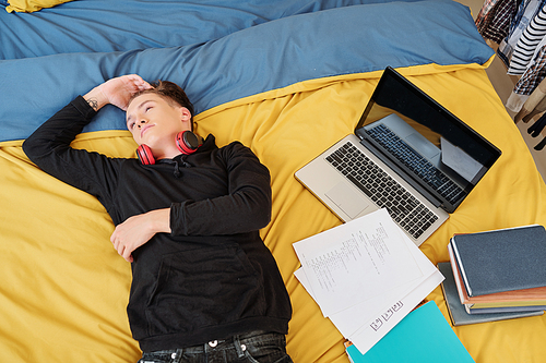 Teenage boy resting on bed tired after studying programming at home