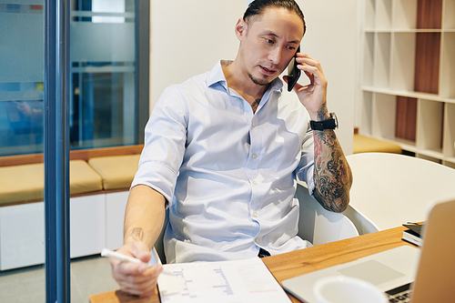 Serious frowning businessman checking documents and talking on phone with colleagues