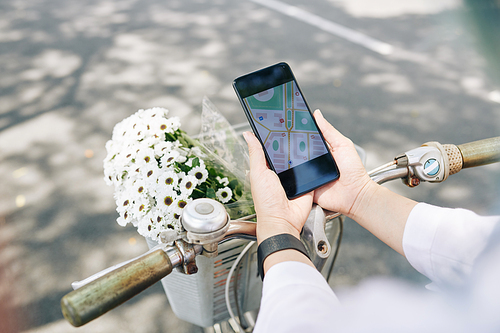 Young woman sitting on bicycle and checking map on smartphone screen