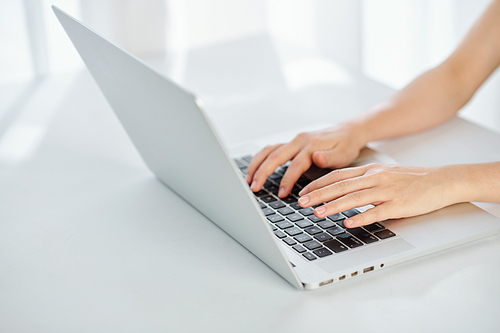 Hands of woman typing on laptop at table in home office due to coronavirus pandemic