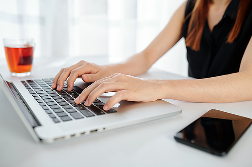 Close-up image of female entrepreneur working on laptop at office desk and drinking black tea