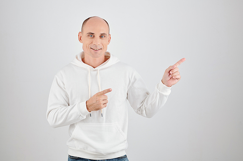 Studio portrait of smiling mature man in white hoodie pointing away