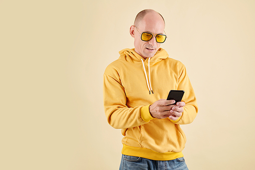 Stylish mature man in yellow hoodie and glasses checking application on smartphone