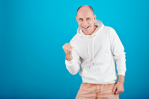 Positive excited mature man clenching fist when celebrating success, isolated on blue
