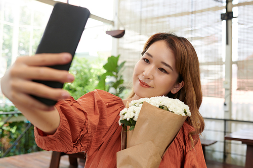 Smiling young woman taking selfie with bouquet of flowers for social media