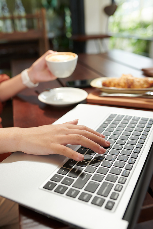 Hands of businesswoman drinking morning coffee in cafe and working on laptop