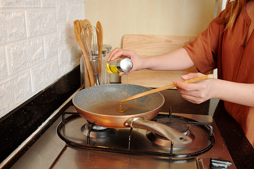 Woman pouring vegetable oil in frying pan when cooking breakfast or dinner in kitchen