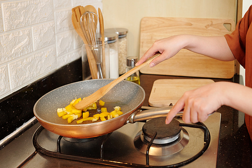 Hands of housewife frying vegetables in pan when cooking delicious dish for dinner