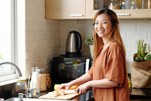 Portrait of smiling attractive young woman cutting bread for breakfast