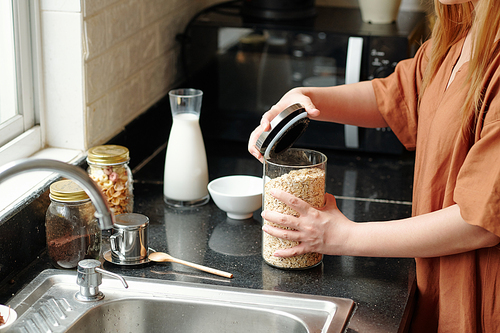 Hands of housewife opening jar of oatmeal jar when cooking breakfast for her family