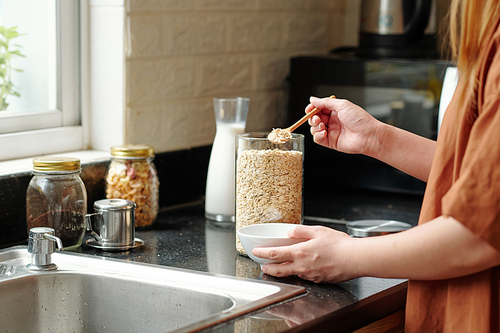 Woman standing at kitchen counter and putting spoon of quick oatmeal in bowl