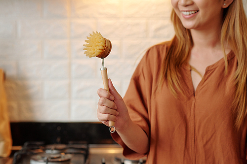 Housewife showing wooden brush with natural bristles she is using for washing dishes