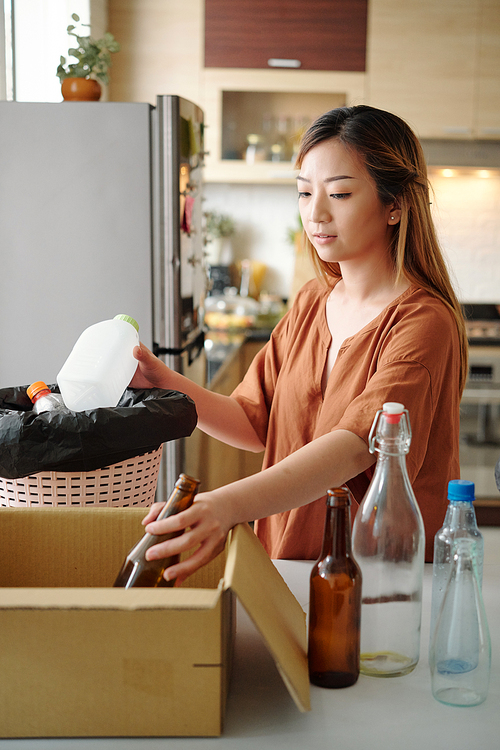 Mindful woman sorting glass and plastics bottles at home and putting in separate bins