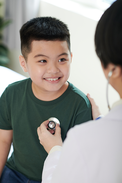 Smiling preteen boy looking at general practitioner who is checking his breath
