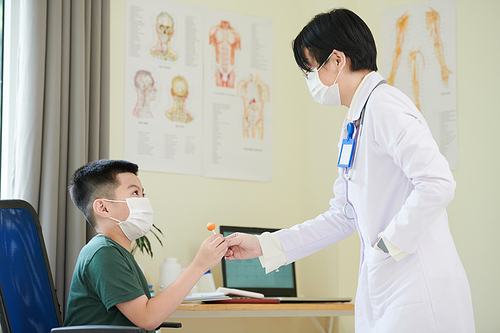 Pediatrician giving lollipop to kid in medical mask afraid of doctors