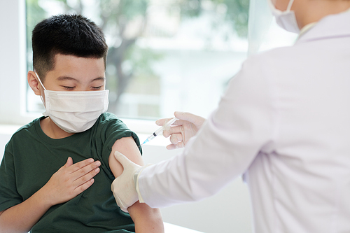 Little boy in medical mask letting doctor to inject vaccine against coronavirus