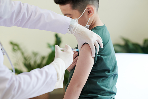 Medical nurse in protective gloves injecting vaccine against coronavirus in arm of preteen boy