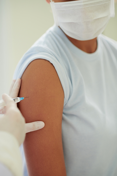 Doctor injecting vaccine against coronavirus in shoulder of teenage girl