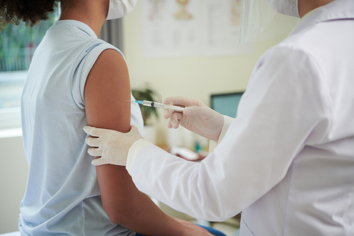 Cropped image of doctor injecting vaccine against coronavirus in arm of teenage girl