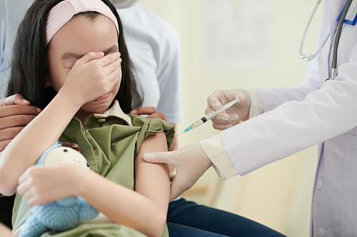 Scared crying girl getting vaccine in medical office to be protected from viruses.