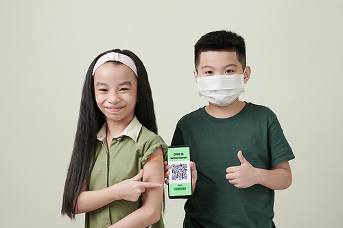 Happy little boy and girl showing smartphone with QR codes after getting vaccine against coronavirus